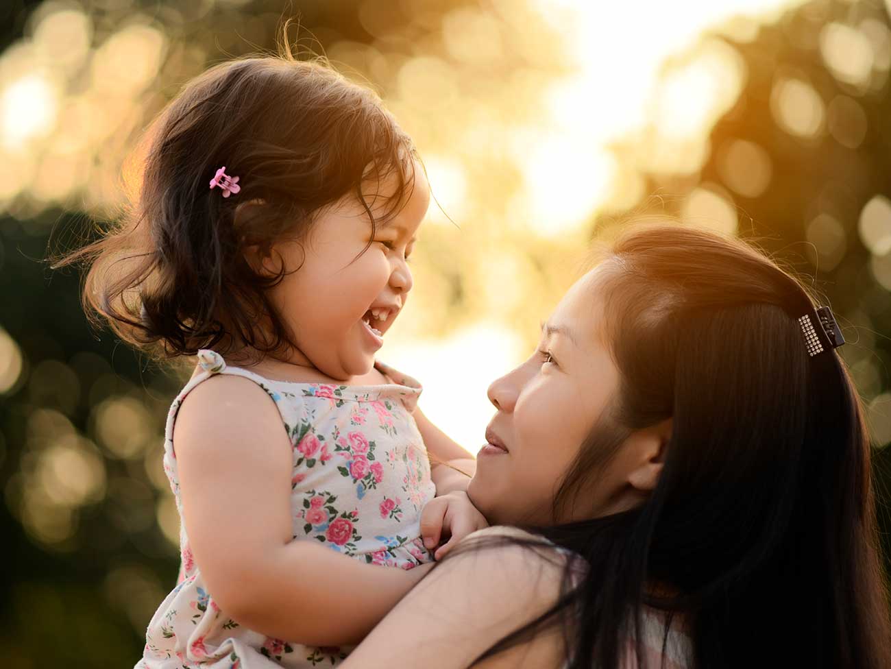 一位年轻的亚洲母亲抱着她笑着蹒跚学步的女儿。