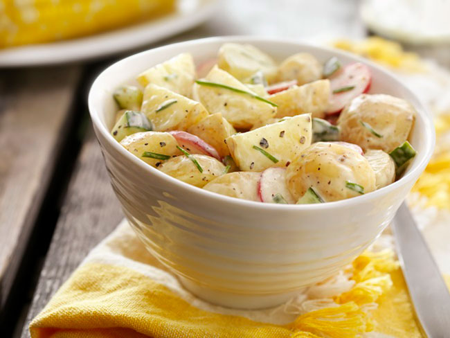 奶油土豆沙拉放在白色的碗里，黄餐巾放在木桌上。