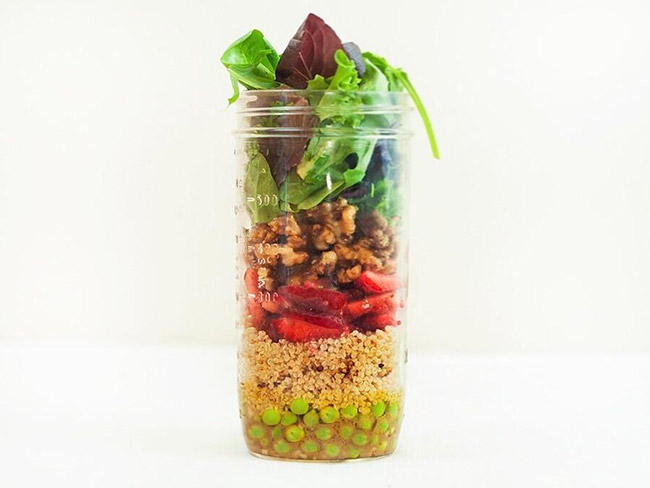 将生菜、坚果、豌豆、藜麦等沙拉原料层层放入一个高大的玻璃罐中。